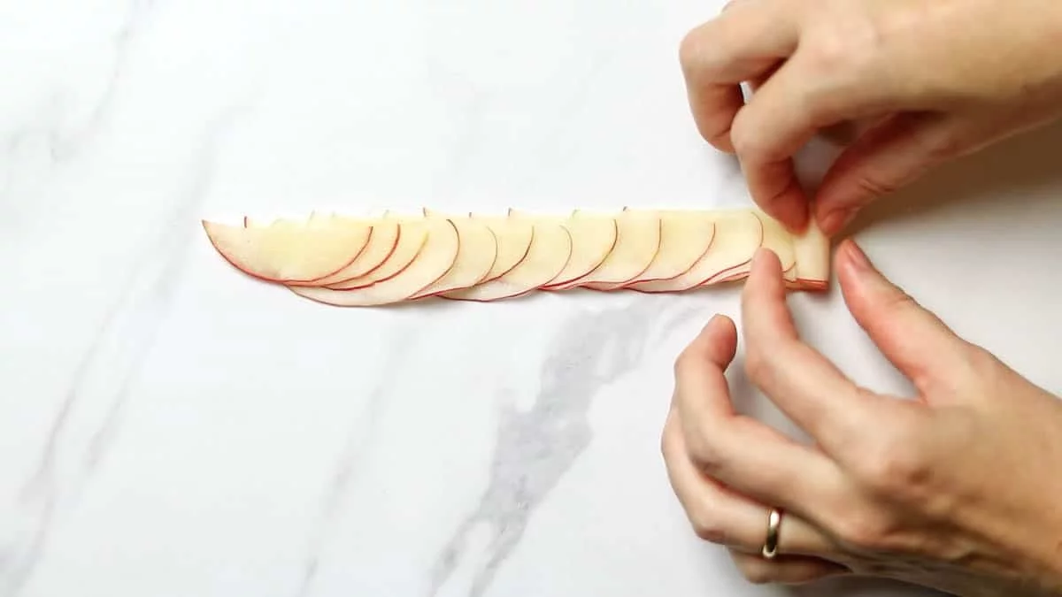 For the final central part, arrange the apple slices on the surface in a circular shape, rolling them up to create small flower-like shapes. Place it in the center and blend it with the surrounding apple slices to create a cohesive design.