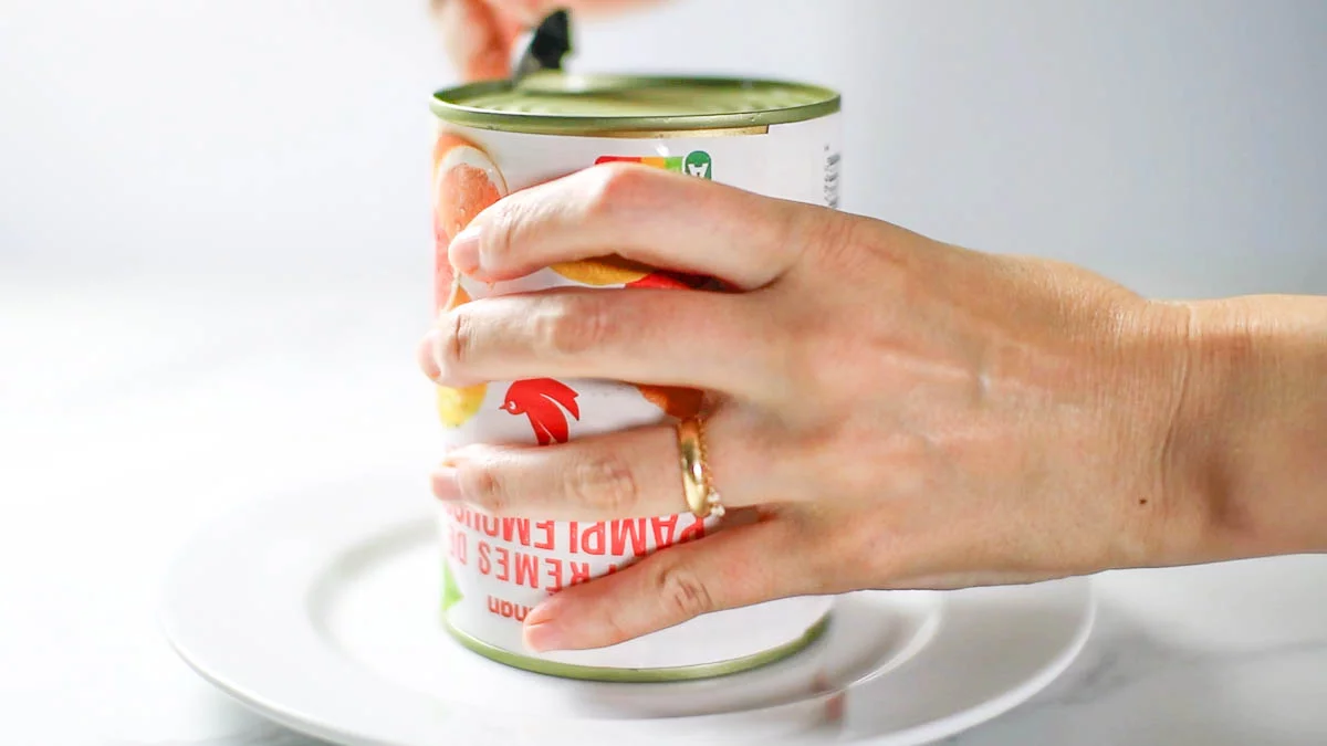 Place a plate on top of the can and flip it over. Use a can opener to make a small hole in the bottom of the can. Allowing air to enter from the bottom will make it easier for the jelly to come out.