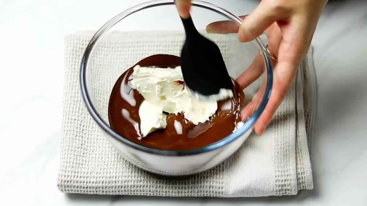 Place the chocolate in a bowl and melt it using either the microwave or a double boiler. Once melted, add the cream cheese and crushed nuts to the chocolate and mix them together.