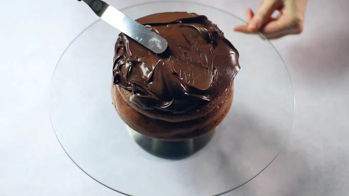 回転台にチョコレートケーキをおきます。表面がでこぼこしているようだったら上面を切り取ります。上から一気にガナッシュをかけて、パレットナイフで上面をならしながらガナッシュを側面に落としてできるだけ均等な厚みになるようにします。