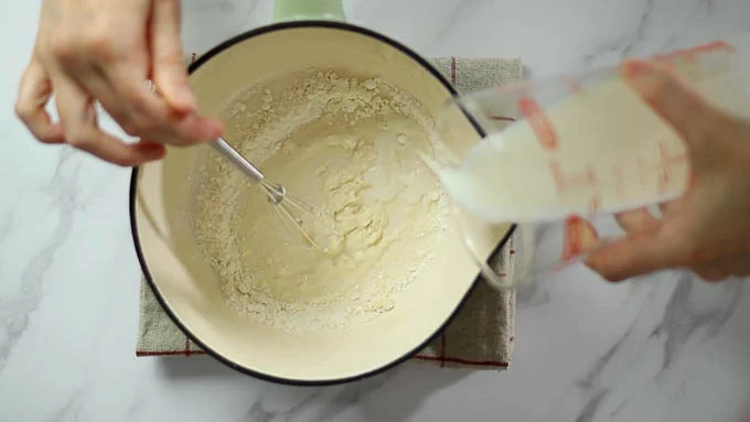 別の鍋に薄力粉とコーンスターチを入れ、牛乳を少しづつ注ぎながらホイッパーで混ぜ溶かします。