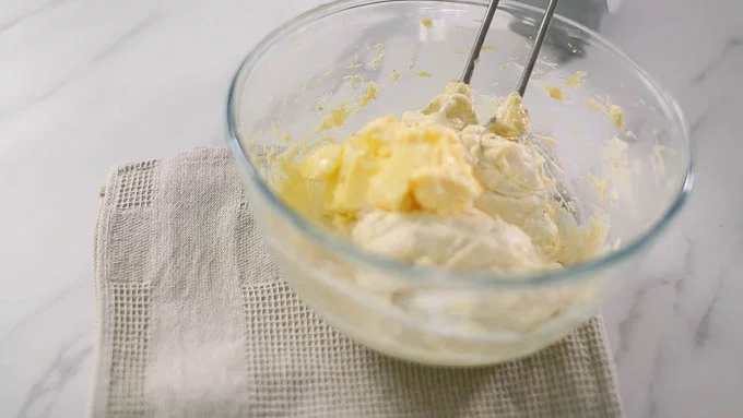 常温に戻した柔らかいバターを少しづつ加えながら、ハンドミキサーで泡立て続けます。黄色いカスタードクリームがだんだんと白っぽくなってきます。