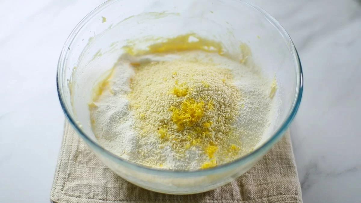 薄力粉とベーキングパウダーをふるい入れ、アーモンドパウダー、レモンの皮を加えてゴムべらで混ぜ合わせます。