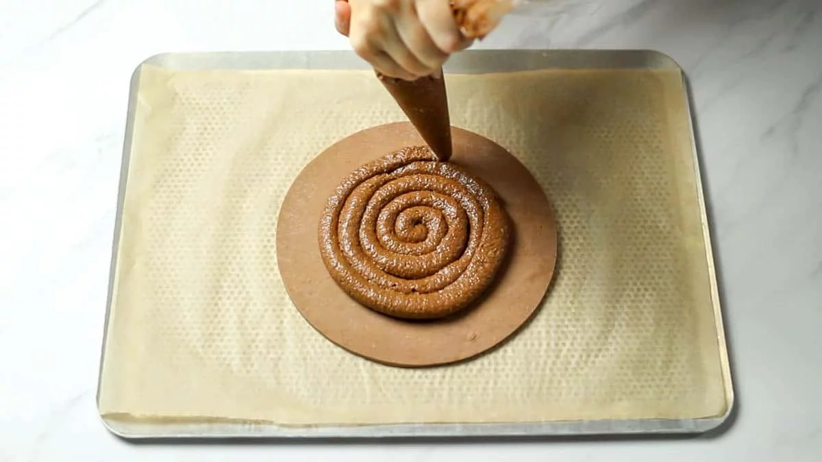 Place a sheet of parchment paper on a baking sheet and place the first pastry dough on it. Pipe the chocolate almond cream in a circular shape on the dough, leaving about a 3cm / 1.2 inches. border. Place the charm (or almond) and lightly press it to embed it.