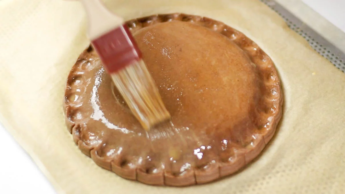 Brush the surface with the beaten egg wash, being careful not to brush over the cut sides where the pastry layers overlap. This can affect the puffiness of the pastry. Place the galette in the refrigerator to allow the egg wash to dry.