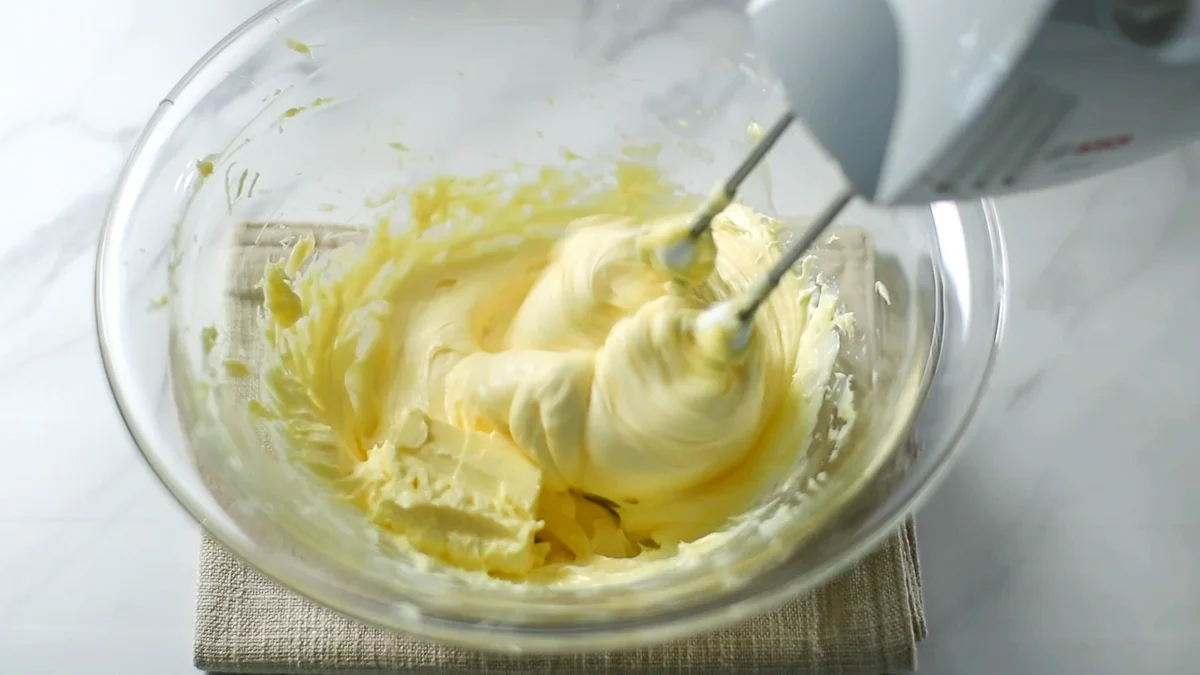 カスタードクリームをハンドミキサーでなめらかにします。 室温に1時間ほど置いて柔らかく戻した柔らかいバターを少しづつ加えながら、ハンドミキサーで混ぜ続けます。
