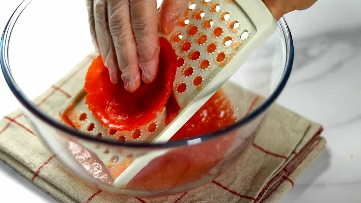 トマトを横半分にカットします。すりおろし器でトマトをカットした断面を下にしてすりおろします（大根おろしみたいな感じです）。すりおろしていくうちに中の果肉の部分だけすりおろされて、最後は皮だけ残ります。
