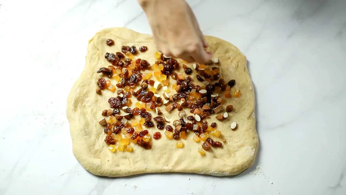 Turn out the dough onto a floured surface Roll out the dough into a square and top with the dried fruit and half of the almonds (Do not add the rum that has not been absorbed by the dried fruits to the dough)