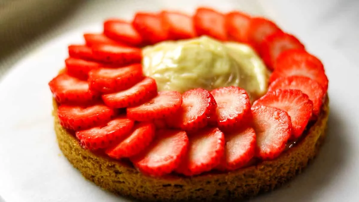 Arrange the sliced strawberries starting with the larger ones, overlapping them in a circular pattern around the edge of the galette. Once you've completed one round around the edge, pour the remaining custard into the center, creating a mound shape. Continue arranging the remaining strawberries in the same way, overlapping them from the outside towards the center, and your galette is ready to serve.