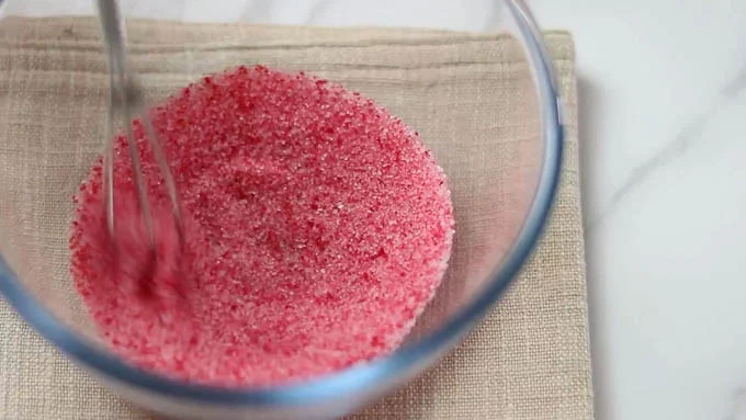 ボウルにグラニュー糖を入れ、赤の食用色素を数滴垂らします。ホイッパーで色が均一になるまでかきませます。