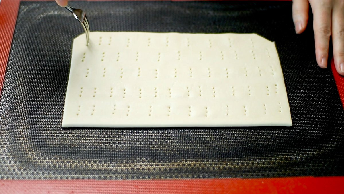 25cm x 35cm の長方形にパイ生地を切り取ります。（パイ生地は多少焼き縮みするので、少し大きくパイ生地をカットしてください。）
シルパンを敷いた天板の上にのせ、全体に空気穴をあけます。冷蔵庫で30分ほど休ませます。